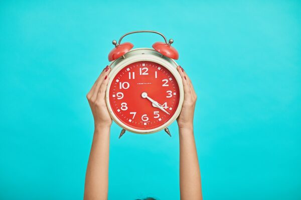 person holding red and beige twin bell analog alarm clock
