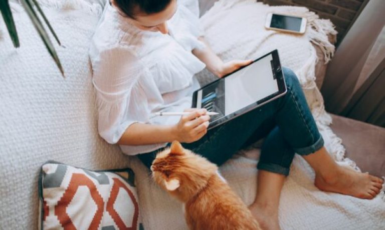 woman in white long sleeve shirt and blue denim shorts sitting on bed using tablet computer