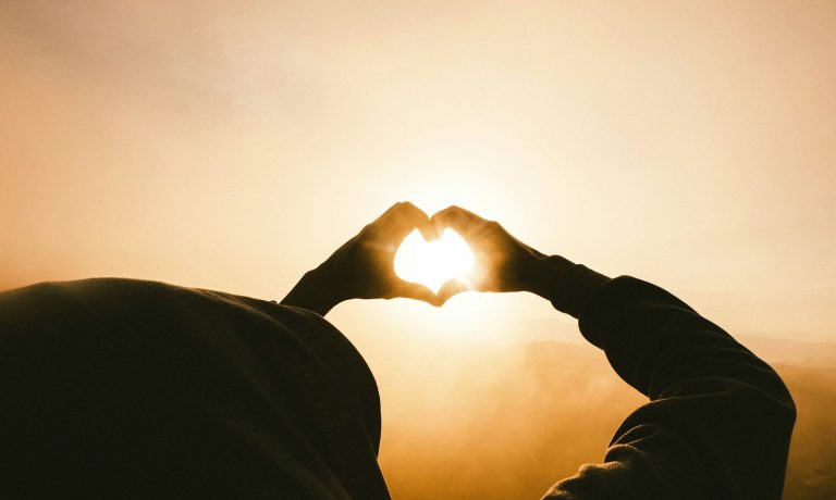 person doing heart shape hand with sun light passing thru